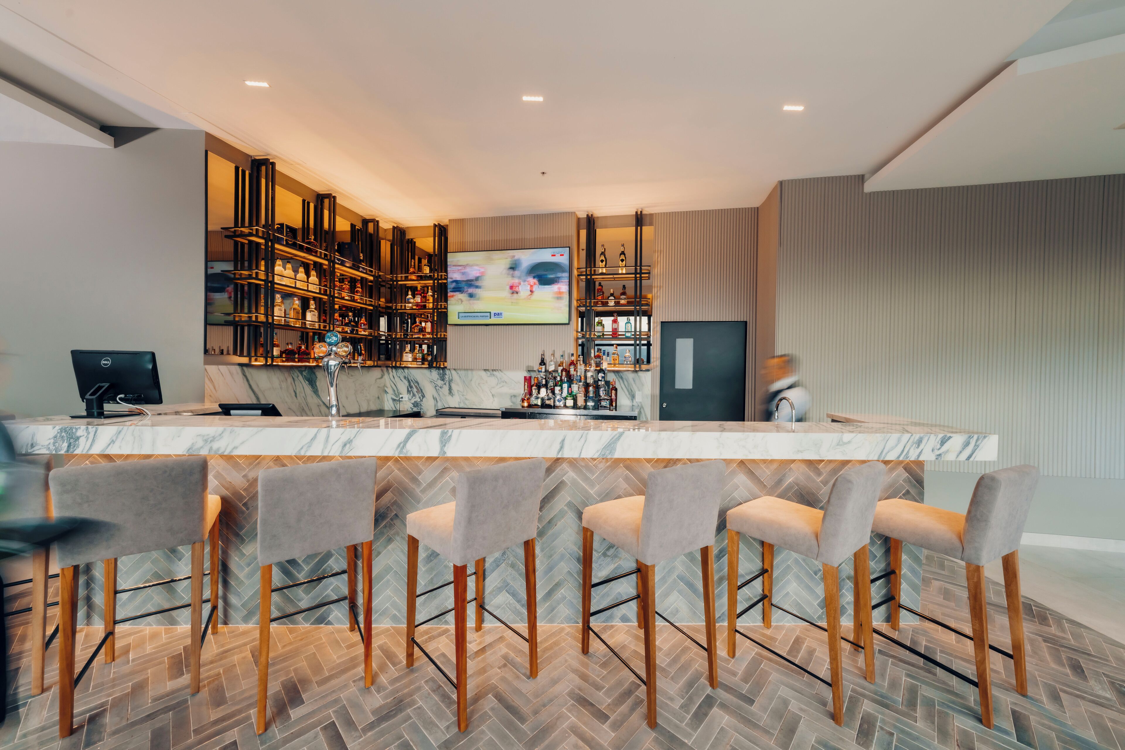 Eine moderne Bar mit Marmorplatte, Barhocker und einem Fernsehbildschirm.