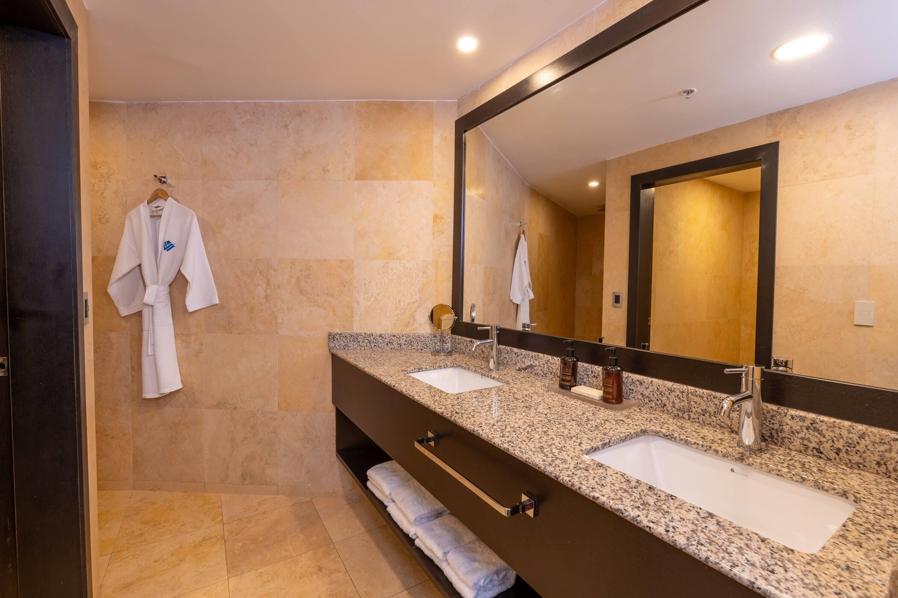 Un baño moderno con dos lavamanos, un espejo grande y una bata colgada en la pared.