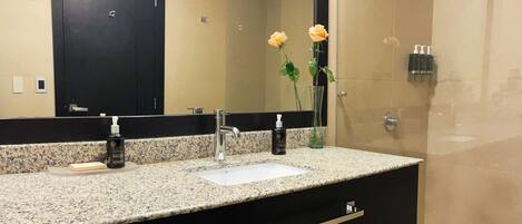 Un baño con encimera de granito, lavabo blanco, mueble negro, espejo y zona de ducha.