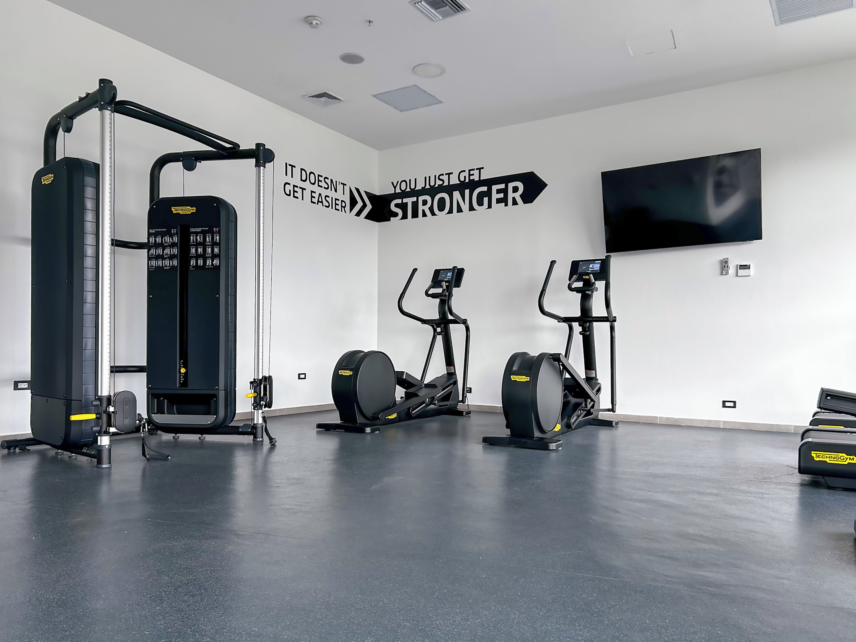 A gym with cardio and strength equipment, motivational wall art, and a flat-screen TV.
