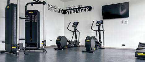 A gym with cardio and strength equipment, motivational wall art, and a flat-screen TV.