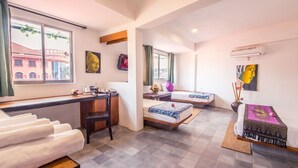 A hotel room with a desk, two beds, a chair, and a window with a view of buildings. - The Purple Mangosteen (Siem Reap)