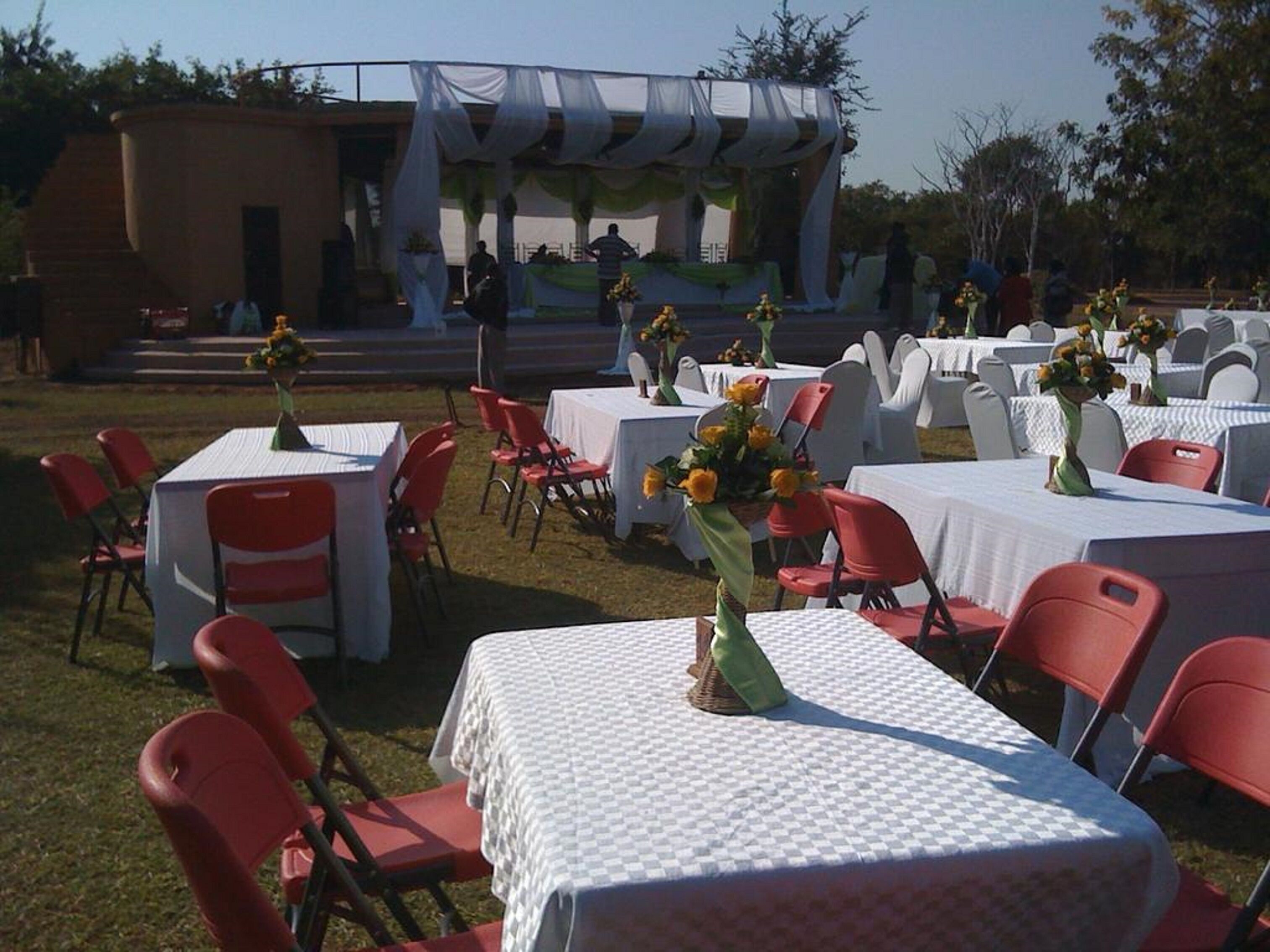 An outdoor event setup with tables covered in white tablecloths, red chairs, and flower centerpieces.