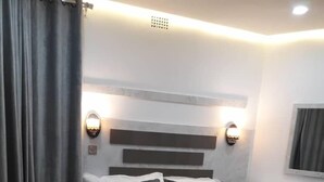 A modern bedroom with a large bed, bedside tables, and a mirror. - Kaazmein Lodge (Livingstone)