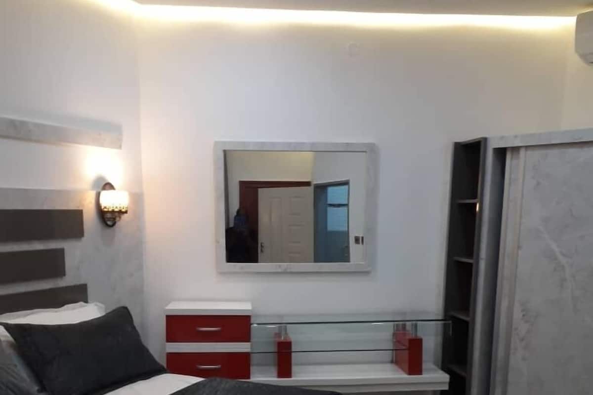 Ein modernes Schlafzimmer mit einem Bett, Nachttischen, einem Spiegel und einem Kleiderschrank.