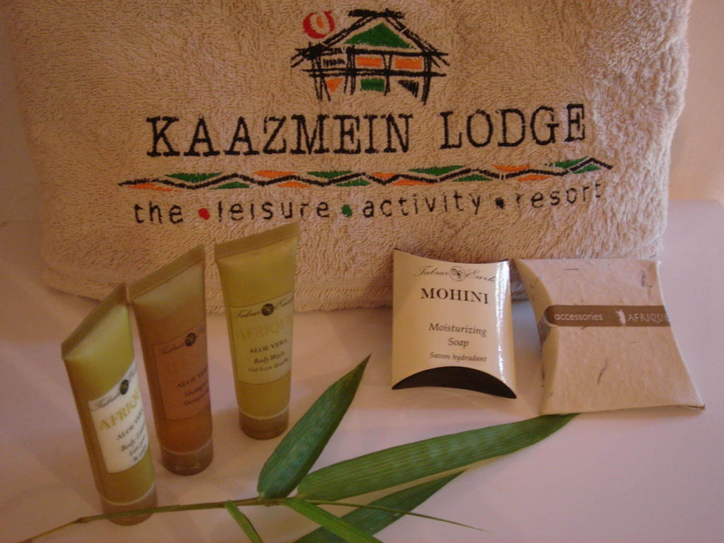 A towel with "KAAZMEIN LODGE" and "the leisure activity resort" text, along with three bottles of body lotion and a bar of soap.