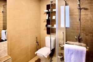 A bathroom with a toilet, a glass shower enclosure, and a shelf with toiletries. - The Dragon Beach Hotel & Resort (Amwaj Islands)