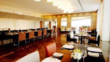 A spacious dining area with multiple tables and chairs, a polished floor, and a high ceiling with pendant lighting.
