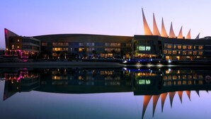 A modern building with a unique architectural design, featuring a large reflective water body in front. - The Dragon Beach Hotel & Resort (Amwaj Islands)
