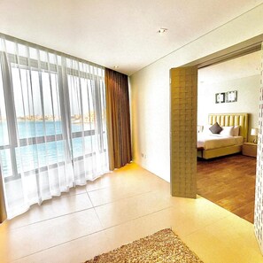 A modern hotel room with a large sliding glass door to a balcony, a bed with a headboard, and a small bedside table. - The Dragon Beach Hotel & Resort (Amwaj Islands)