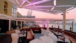 A rooftop restaurant with outdoor seating, a view of the city, and a modern architectural design. - The Dragon Beach Hotel & Resort (Amwaj Islands)