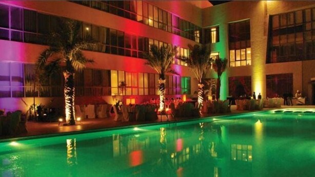 Ein Hotel mit Swimmingpool, Palmen und einer gut beleuchteten Fassade.