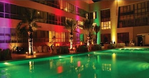 A hotel with a swimming pool, palm trees, and a brightly lit facade. - The Dragon Beach Hotel & Resort (Amwaj Islands)