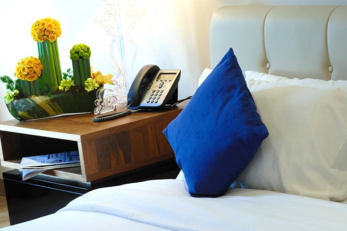 Ein Hotelzimmer mit einem Bett, einem Nachttisch aus Holz, einem Telefon und einer dekorativen Vase mit Blumen.