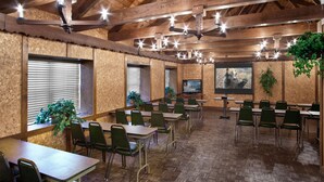 A conference room with wooden walls, green chairs, tables, a TV screen, and hanging plants. - Helendorf River Inn, Suites & Conference Center (Helen)