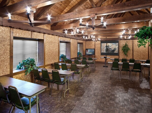 A conference room with wooden walls, green chairs, tables, a TV screen, and hanging plants.