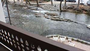 A view of a river with rocks and trees, a metal railing, and white chairs on a brick path. - Helendorf River Inn, Suites & Conference Center (Helen)