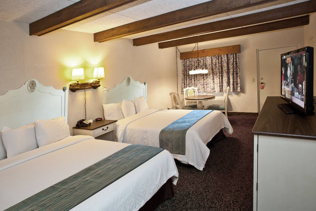 A hotel room with two beds, a desk, a television, and a dining area.