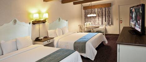 A hotel room with two beds, a desk, a television, and a dining area.