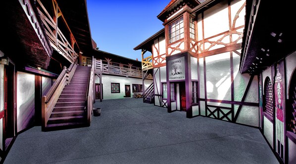 A courtyard with a staircase leading to a second floor, surrounded by buildings with traditional architecture and a sign reading "Grimms' Court Yard".