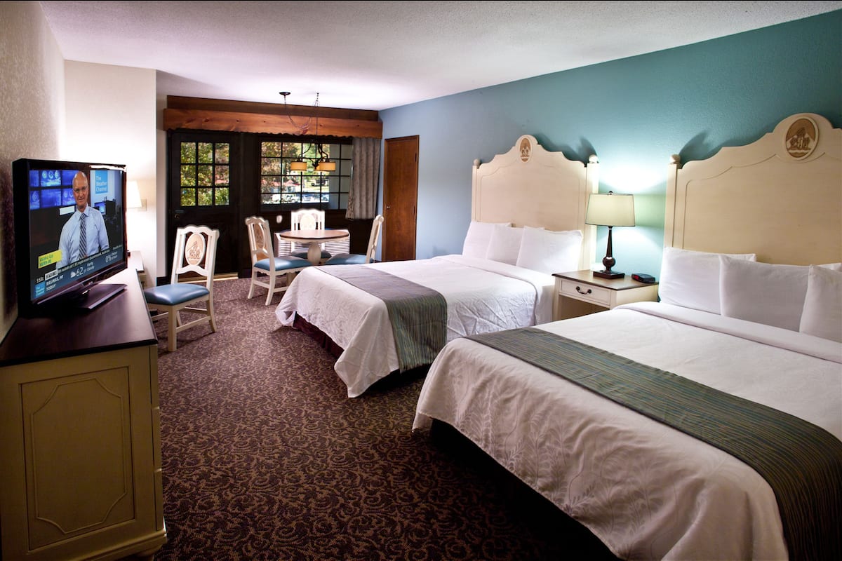 A hotel room with two beds, a television, a desk, and a chair.