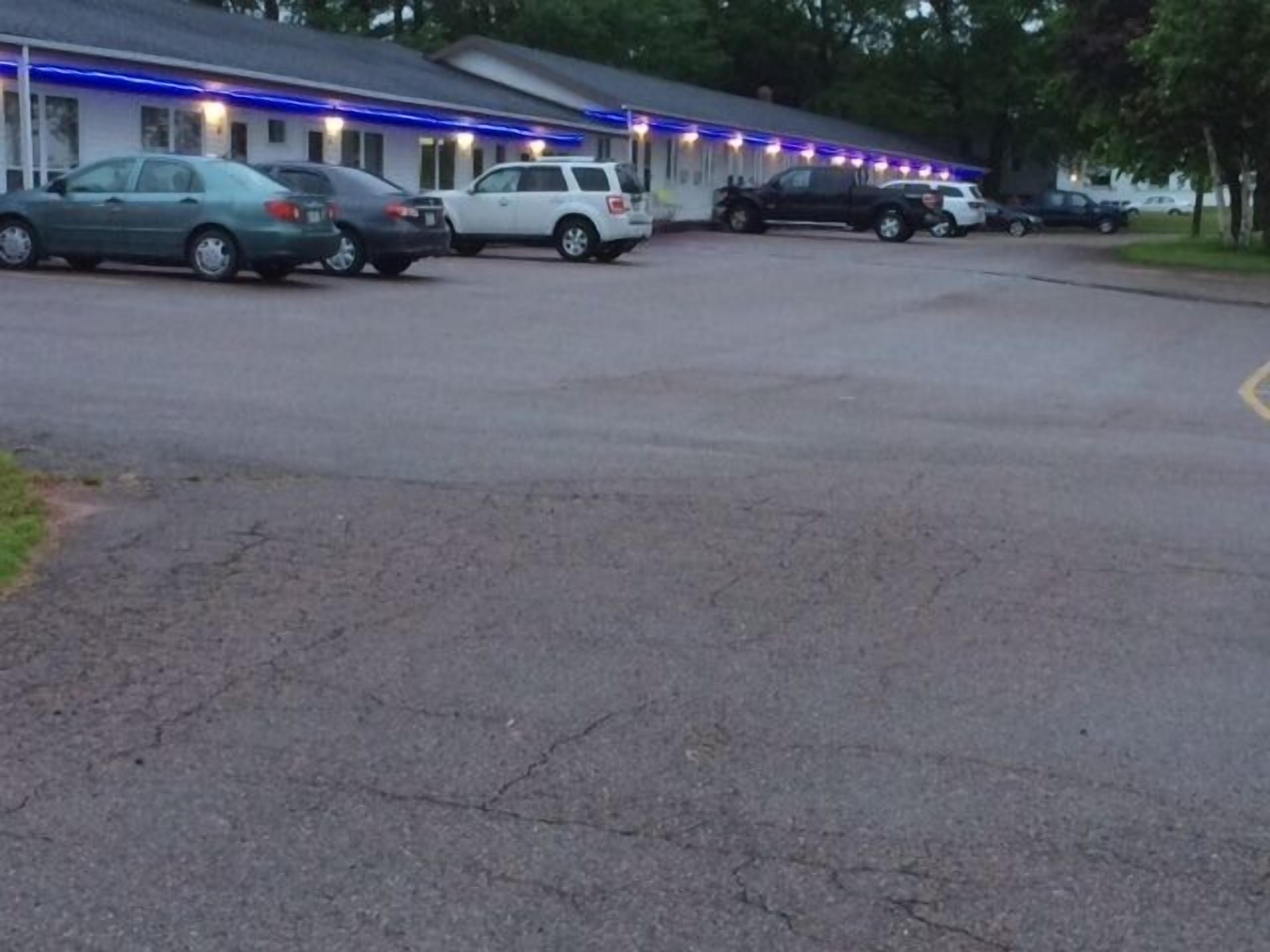 A motel with multiple parking spaces and a row of rooms with blue exterior lighting.