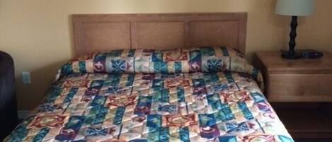 Una cama con un colcha colorida, una mesita de noche con una lámpara y un cuadro en la pared.
