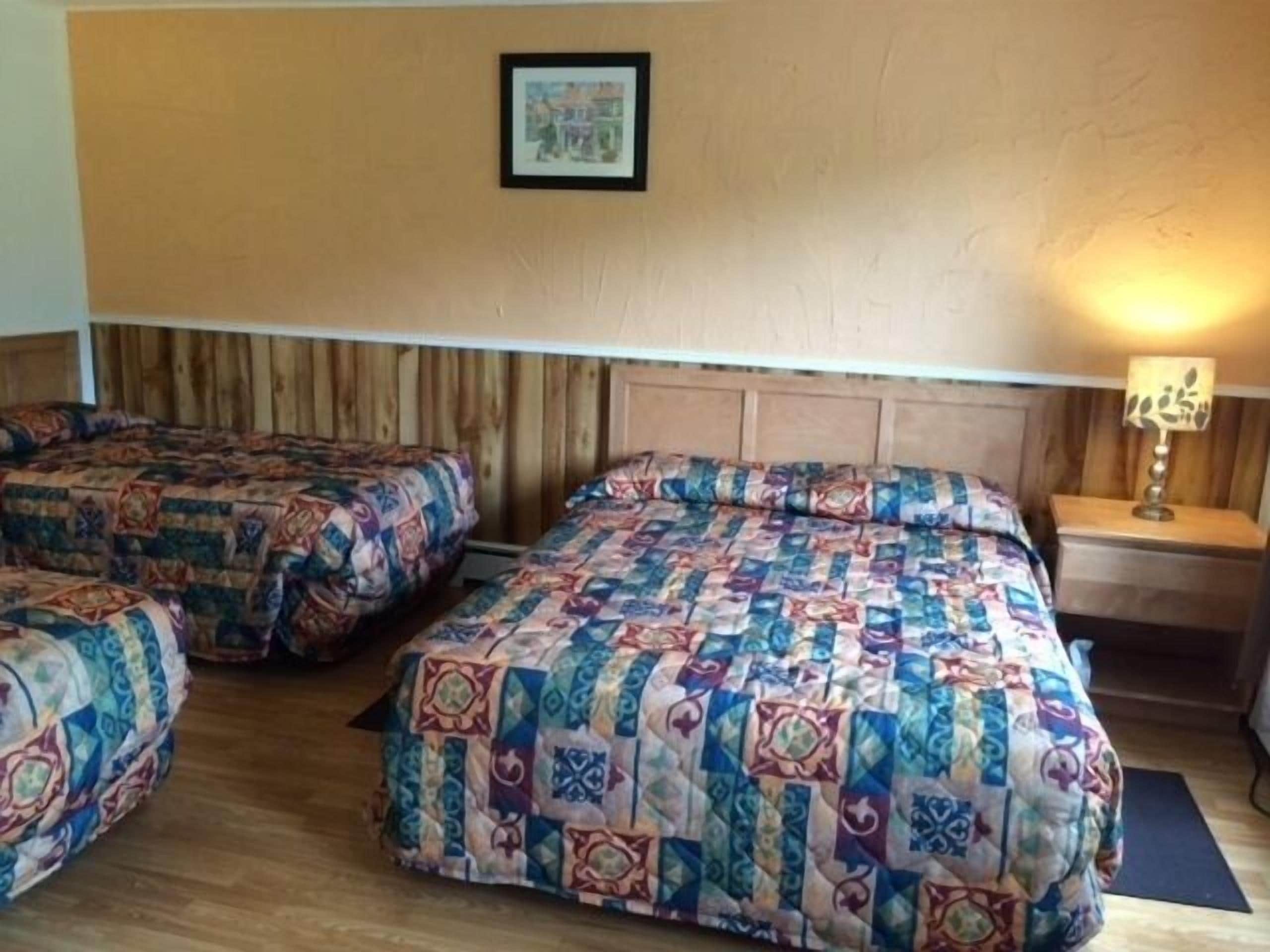 Ein Zimmer mit zwei Betten, jedes mit einer farbenfrohen Steude, einem Holz-Kopfteil, einem gerahmten Bild an der Wand und einer Nachttischlampe.