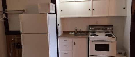 Una cocina funcional con armarios blancos, un refrigerador, una estufa y un lavamanos.