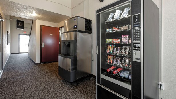A vending machine with snacks and a refrigerator in a hallway. - Red Roof Inn Vermillion - U of South Dakota (Vermillion)