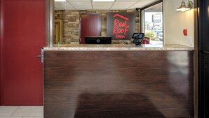 A reception desk with a stone wall backdrop, a Red Roof Inn sign, and a Dell computer monitor. - Red Roof Inn Vermillion - U of South Dakota (Vermillion)