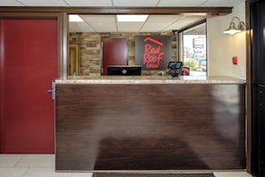 Ein Empfangsschalter mit einer Wand aus Stein im Hintergrund, ein Schild des Red Roof Inn und ein Dell Computer-Monitor.