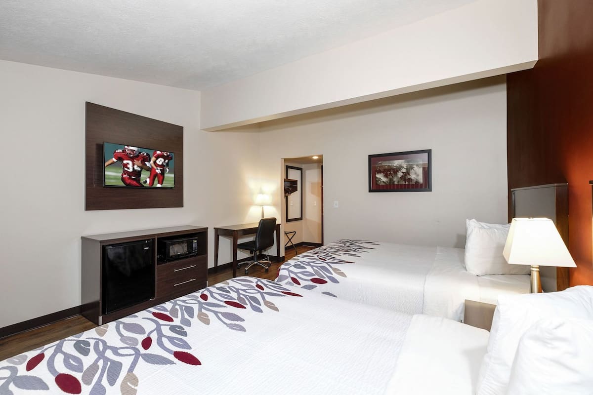 A hotel room with two beds, a desk, a TV, and a lamp.