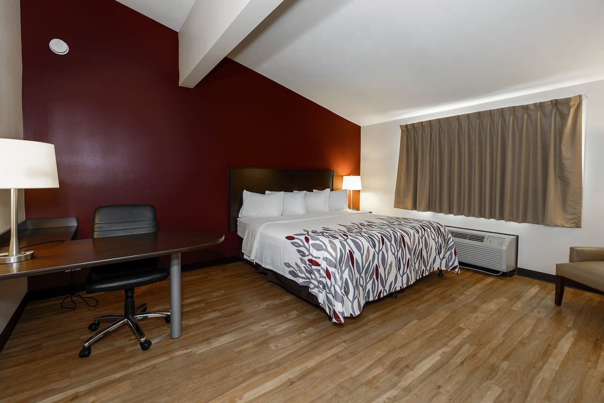 A hotel room with a bed, a desk, a chair, a lamp, and a window with curtains.