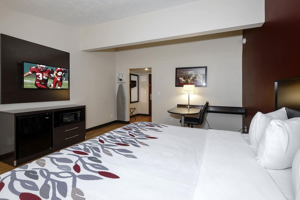 A hotel room with a bed, a desk, a television, and a mirror.