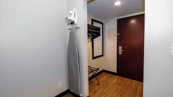 Un pasillo con suelo de madera, pared blanca, puerta oscura y un espejo.