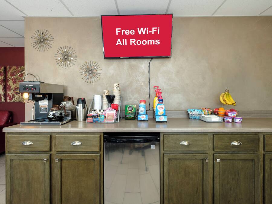 A hotel reception area with a coffee station, a flat-screen TV displaying 'Free Wi-Fi All Rooms,' and various food and drink items.