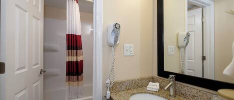 A bathroom with a shower, a sink, a mirror, and a hairdryer.