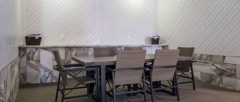 Un comedor con una mesa larga y sillas, un salpicadero de mármol y cestas de mimbre en la pared.