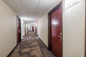 A hotel corridor with carpeted floors, doors on both sides, and an exit sign on the ceiling.