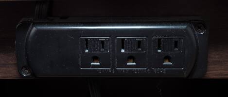 Un enchufe eléctrico negro con tres tomas, un tornillo a la izquierda y un cable conectado.