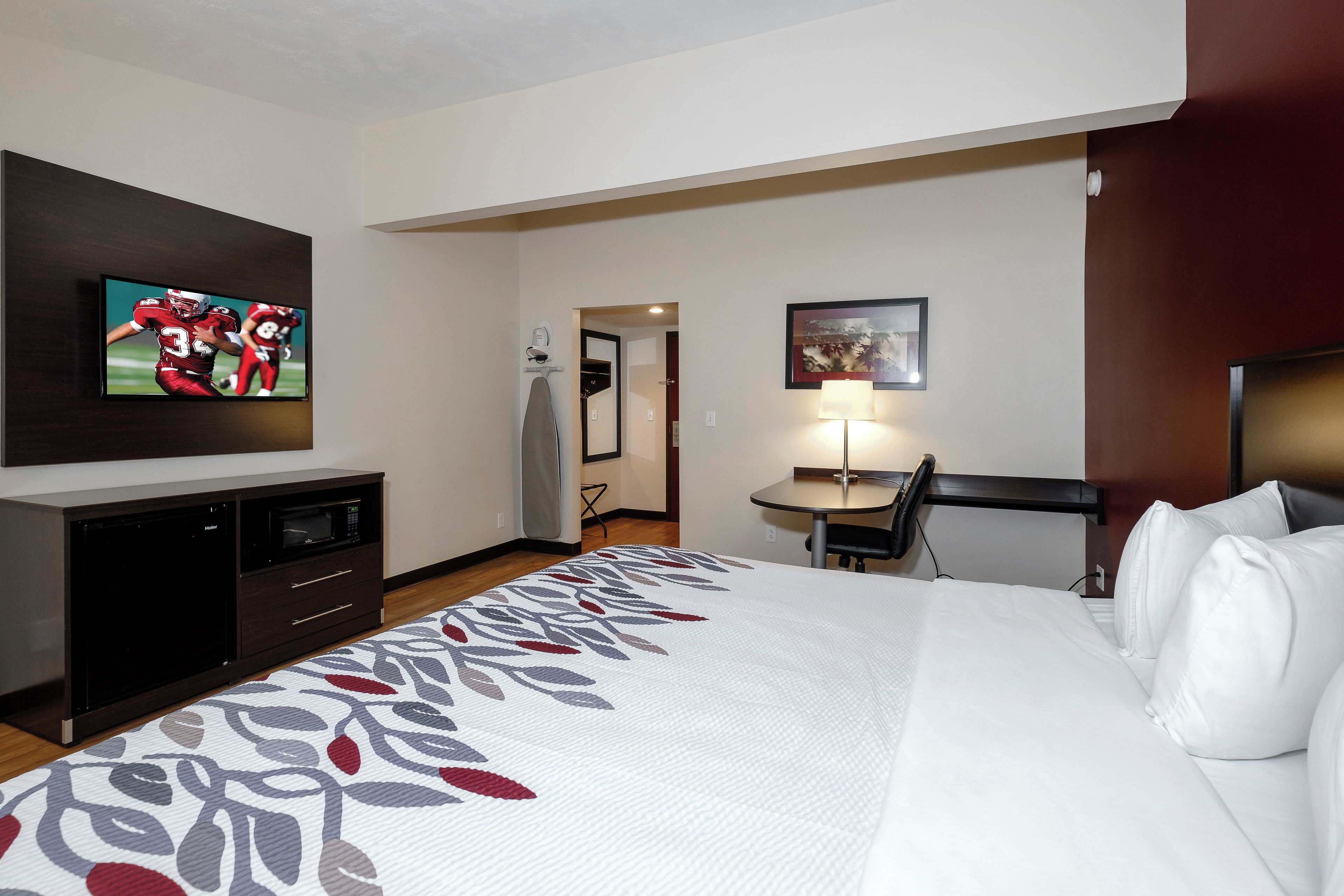 A hotel room with a bed, a desk, a chair, a television, and a microwave.