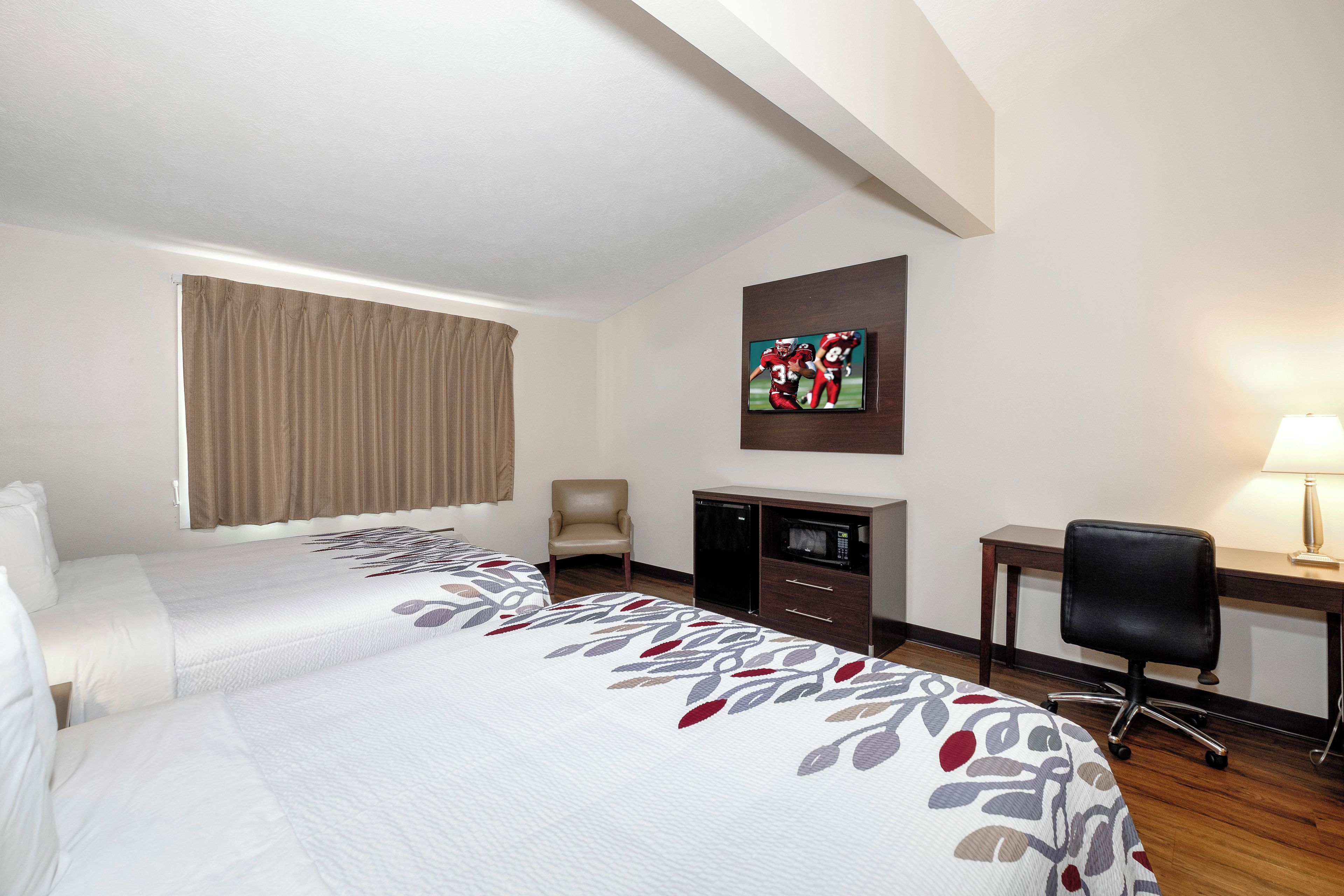 A hotel room with two beds, a desk, a chair, a television, and a window with curtains.