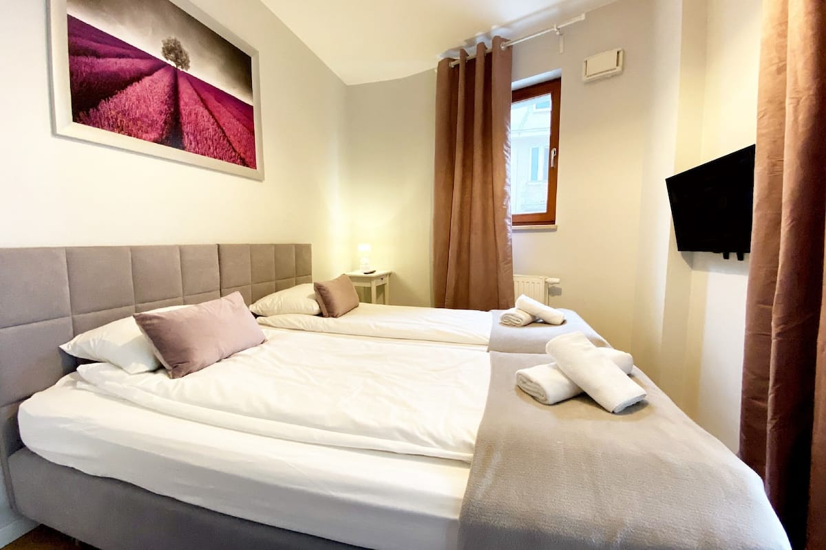 A hotel room with two beds, a flat-screen TV, a painting on the wall, and a window with curtains.