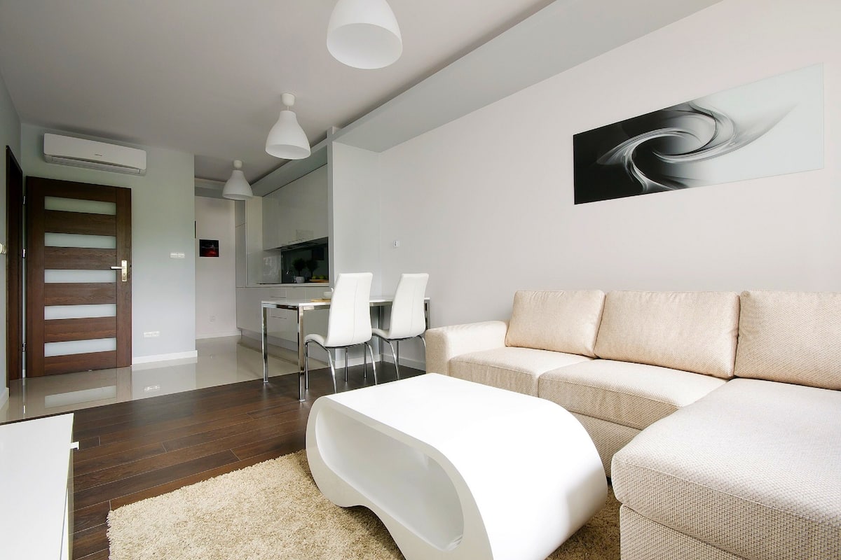 A modern living room with a sofa, a white coffee table, and a dining area with chairs.