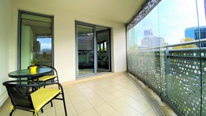 Un balcon avec une porte-fenêtre, une petite table avec des chaises et une vue sur le paysage urbain.
