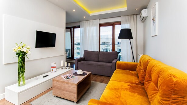 Un salon moderne avec un canapé, une table basse, un téléviseur fixé au mur et une fenêtre avec des rideaux.