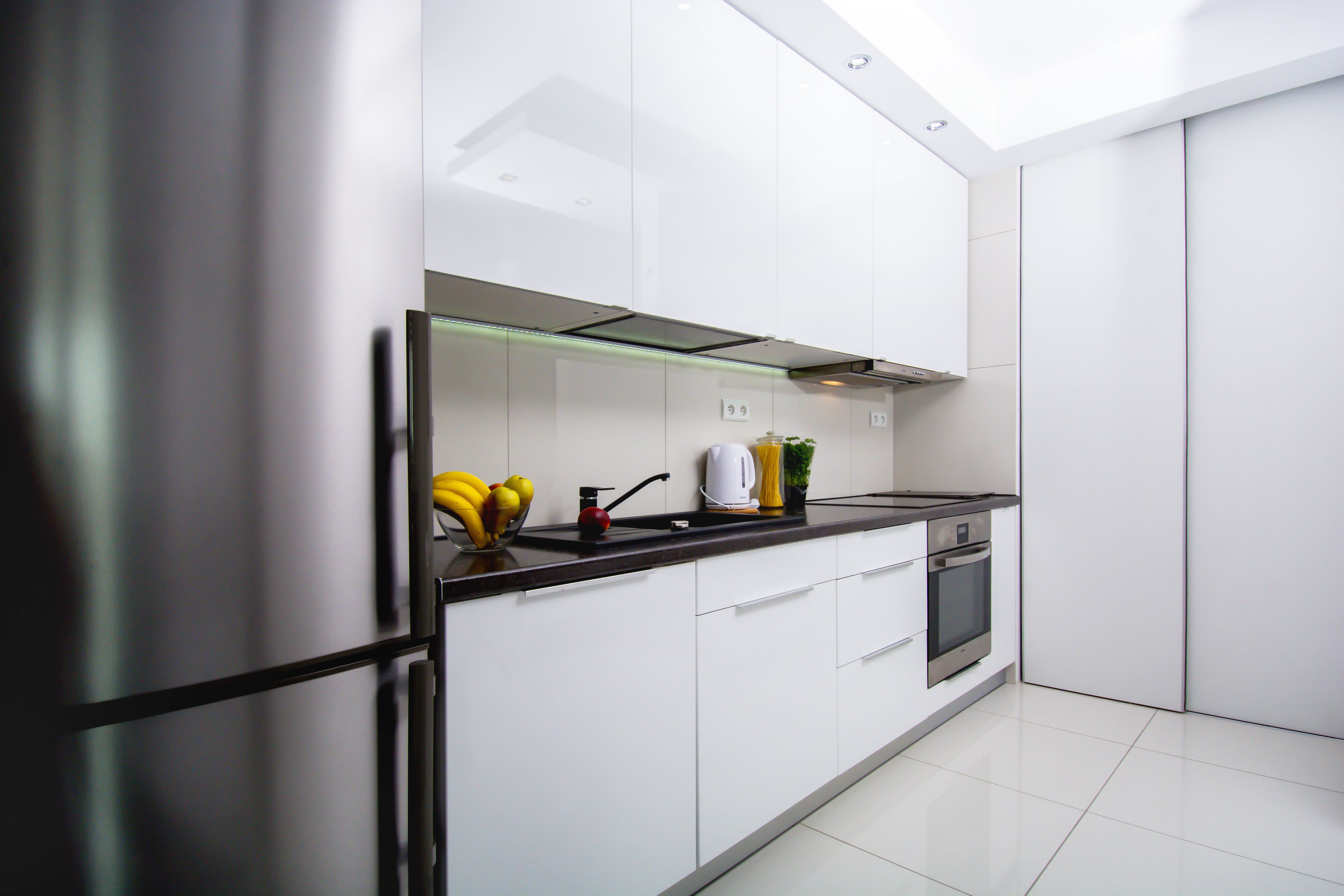 Una cocina moderna con armarios blancos, un refrigerador de acero inoxidable, una encimera negra y un horno empotrado.