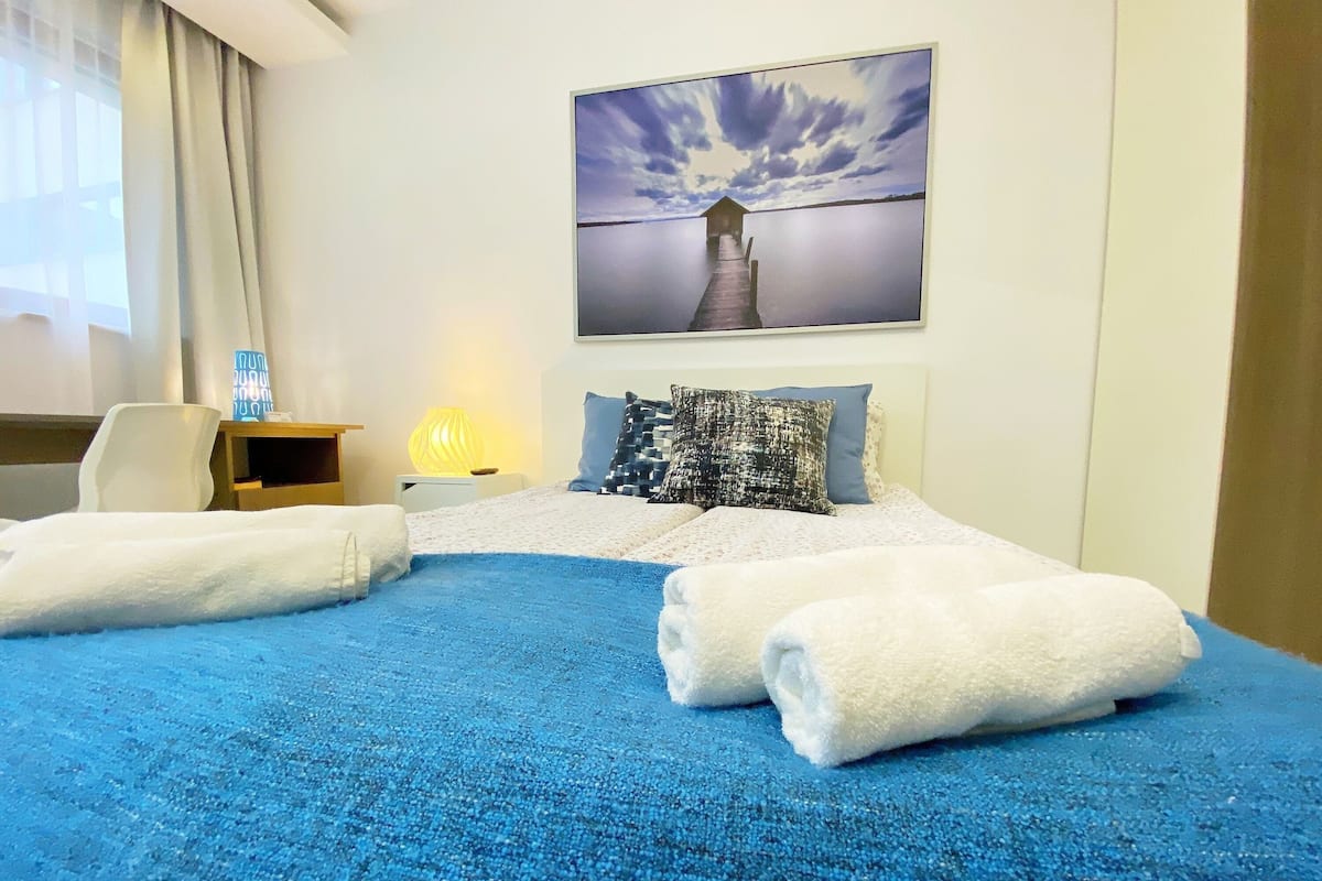 A hotel room with a bed, a desk, a chair, and a painting of a pier.