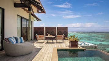 A wooden deck with a pool, a round seating area, and a table with chairs.